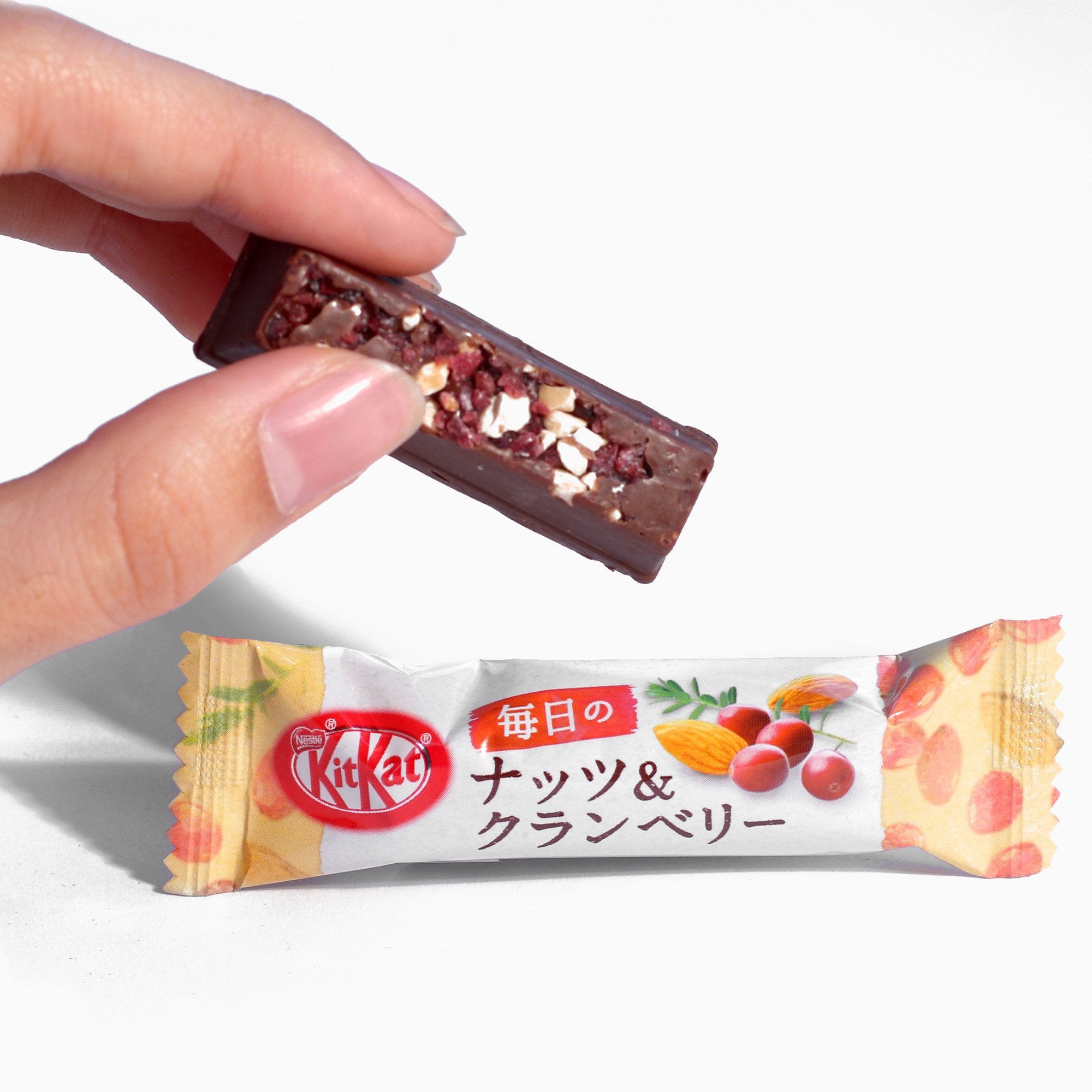 An opened Almond & Cranberry Kit Kat Chocolate Bar being held with hand and the other as a singular unopened Almond & Cranberry Kit Kat Chocolate Bar.